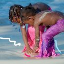 Duas meninas com caudas de sereia brincam com areia em uma praia
