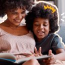 Mãe e filho, ambos negros e com cabelos crespos e penteado black power, estão sorrindo e lendo um livro