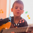 Um menino toca violão e canta. Ao redor, estão desenhadas notas musicais
