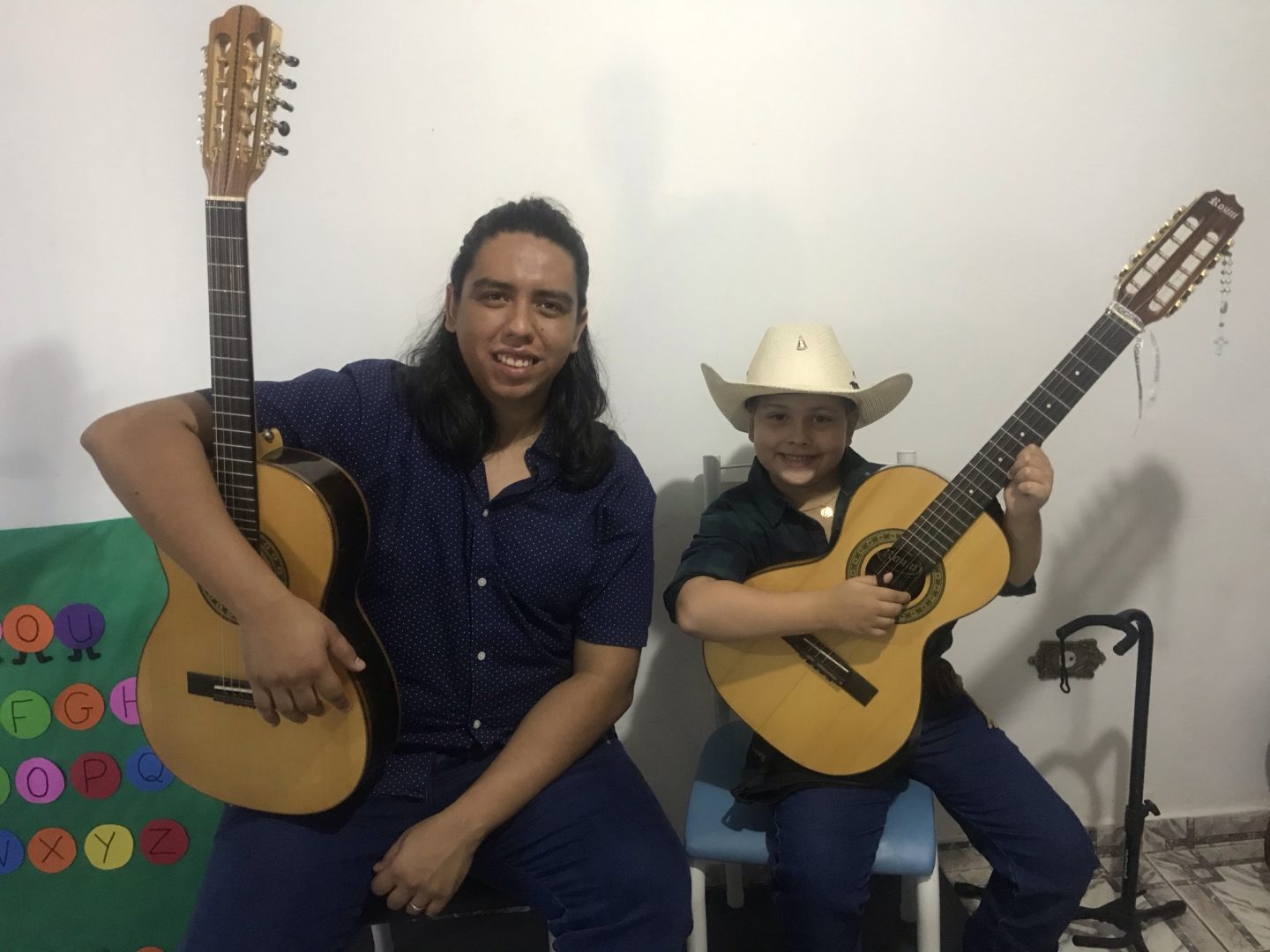 Música sertaneja e infância: Um menino com chapéu e violão está ao lado de um homem, também segurando violão