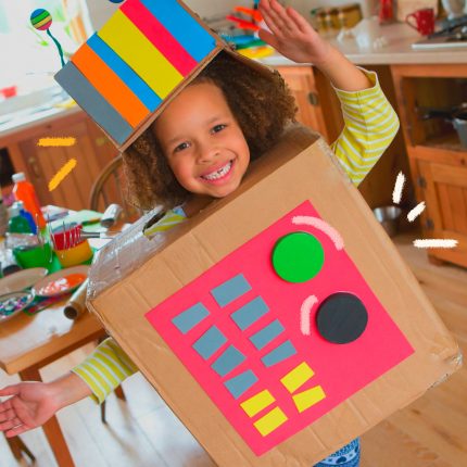 Brincadeiras para reciclagem: Uma menina, de pele negra e cabelos crespos, está dentro de uma caixa de papel e usando um chapéu feito de caixa e papel colorido