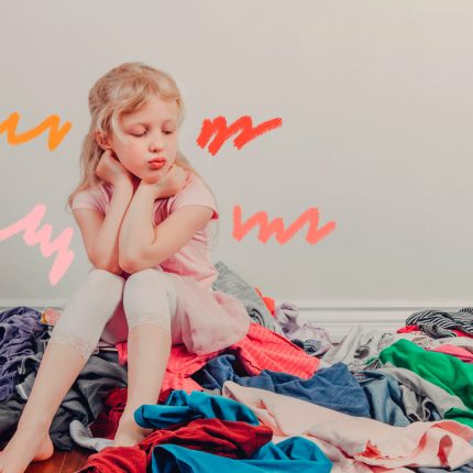 Depressão e consumismo: Uma menina está sentada em cima de uma pilha de roupas e olha para elas com uma expressão chateada