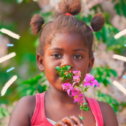 Uma menina com o cabelo preso em três partes segura um ramo de primavera em frente ao rosto. A matéria é sobre brincadeiras com elementos da natureza