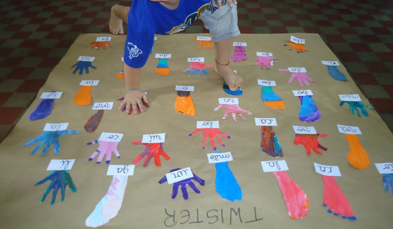 Mãos e pés de uma criança cobrindo algumas letras em um jogo de twister