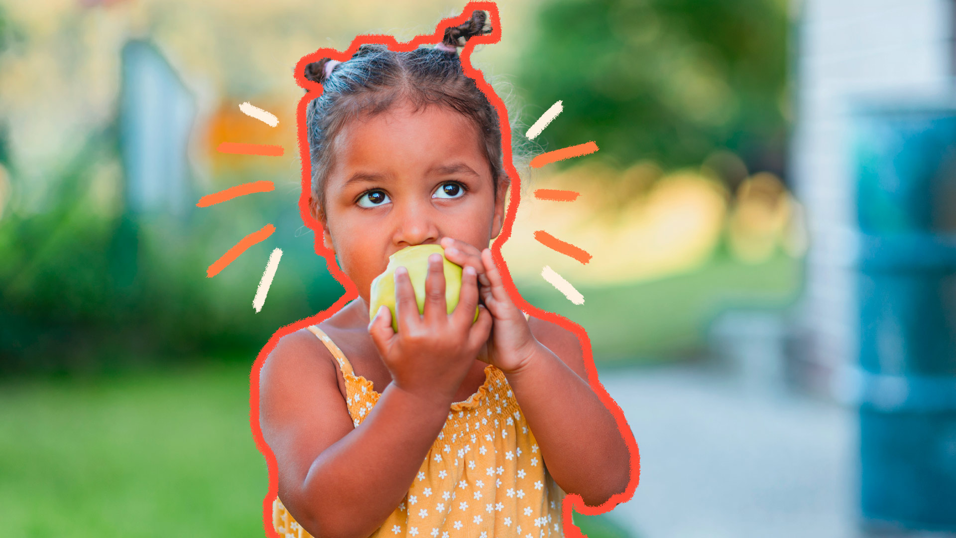 Foto de uma criança que segura uma fruta com as duas mãos e a morde. Ela veste uma blusa com estampa de estrelinhas