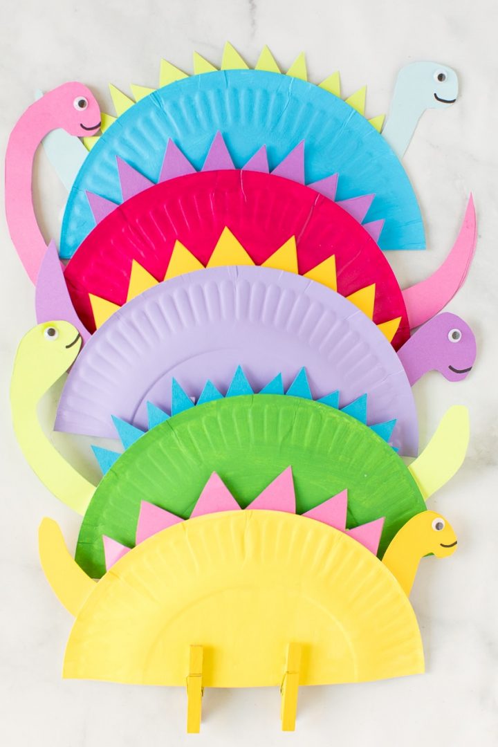 Brincadeiras de dinossauros: pratinhos de papel colorido dobrados ao meio, com espigas de papel coloridas ao redor e cabeças e rabos recortados de dinossauros nas pontas