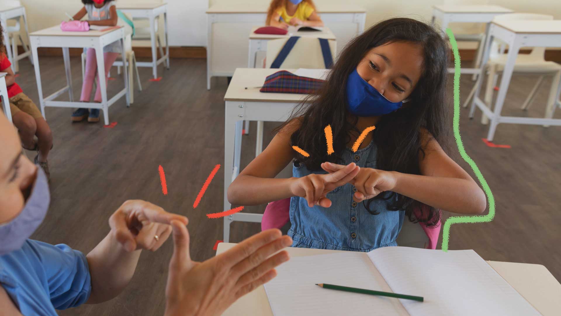 Uma menina de cabelos pretos e lisos, usando máscara de proteção respiratória, está sentada em uma carteira em uma sala de aula, se comunicando por Libras com outra pessoa à sua frente (só aparece as mãos)
