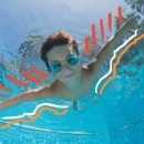 Um menino de braços abertos nadando em uma piscina