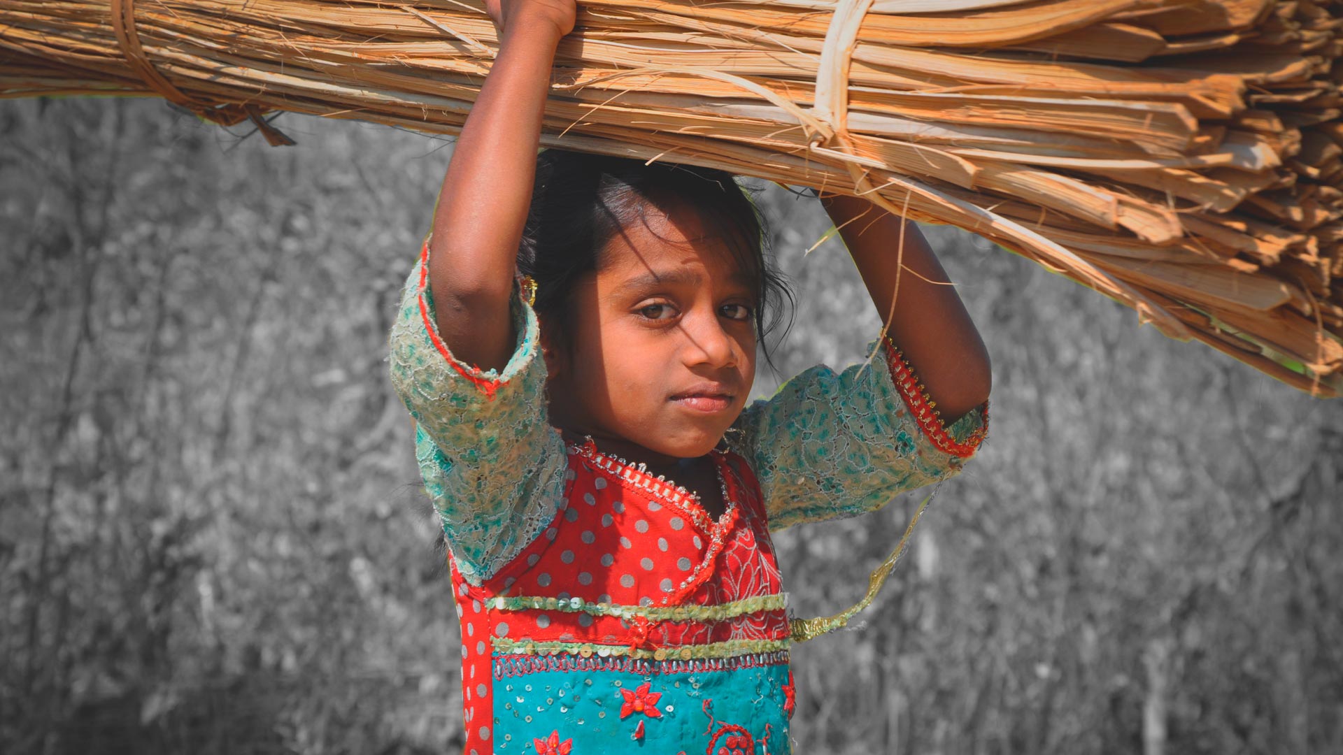 Trabalho infantil: Foto de uma menina com vestido colorido que carrega produtos acima da cabeça