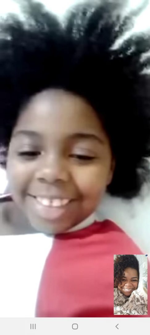 Print de uma videochamada por celular: na tela menor, está uma mulher negra (Eliana), de cabelos crespos e curtos, sorrindo. Na tela maior, uma menina negra de cabelos crespos e curtos, também sorrindo.