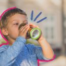 Foto de um menino branco de cabelo loiro bebendo uma latinha de refrigerante