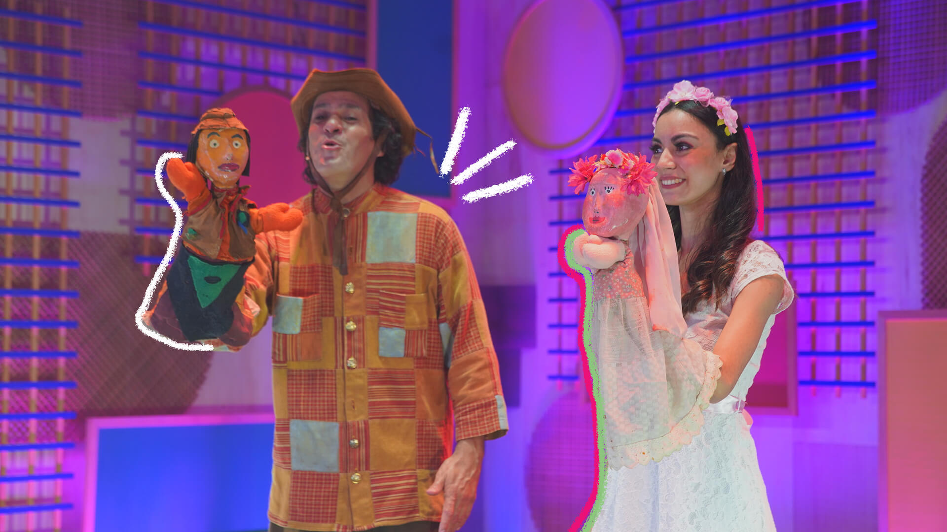 Na foto, um ator e uma atriz, ambos de pele clara, sorriem enquanto realizam show teatral com bonecos