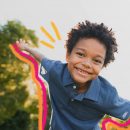 Foto de um menino negro, sorrindo, de braços abertos, como se estivesse voando ilustra o tema da autonomia das crianças.