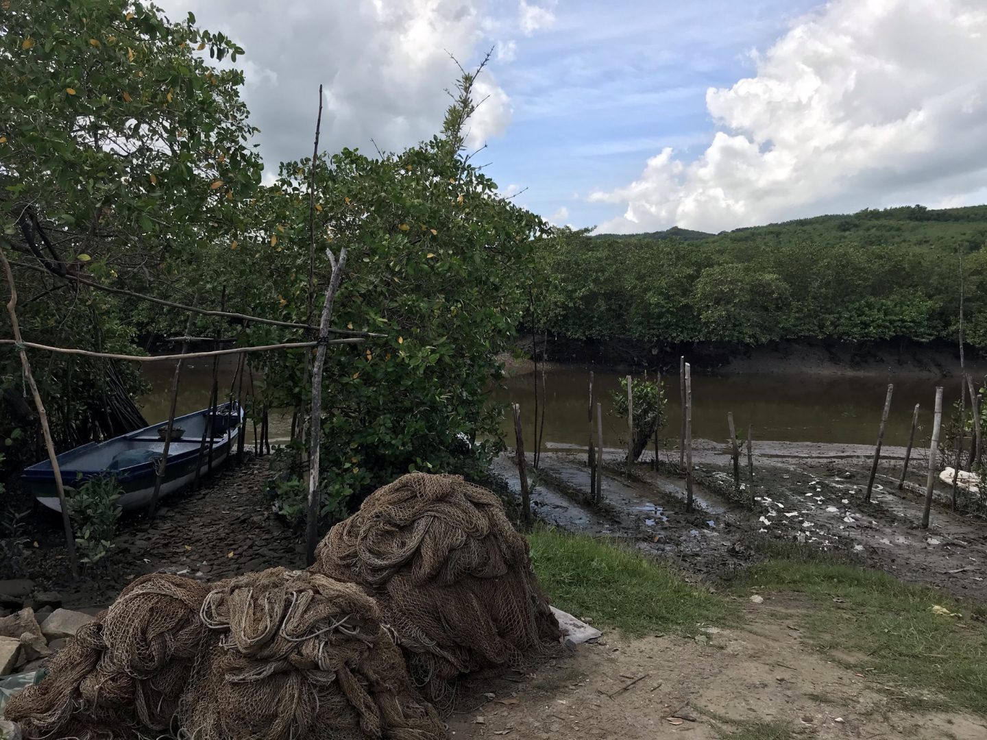 Três montes de redes de pesca artesanal em frente a uma canoa, na beira de um rio.