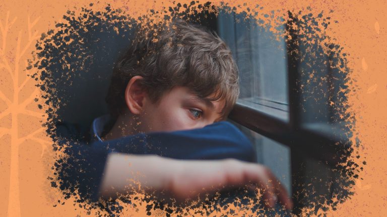 Um menino, de pele branca, está olhando pela janela, com semblante aparentemente preocupado e triste