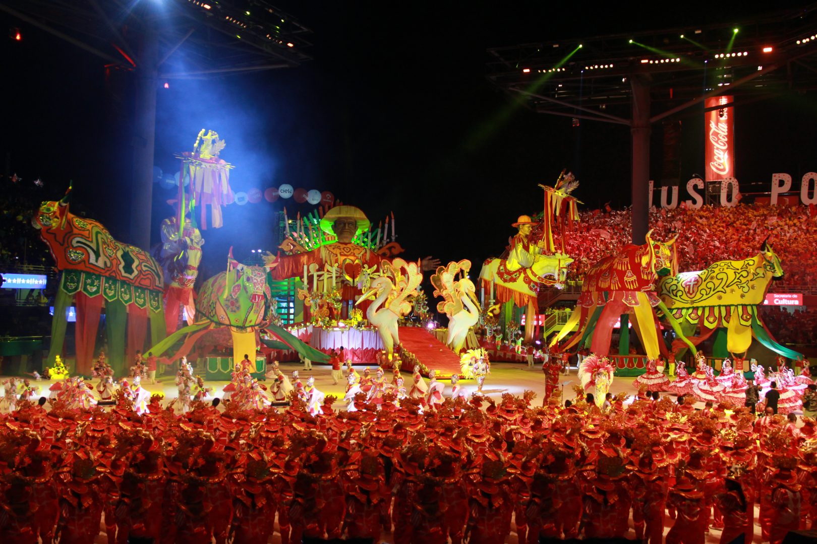 Foto de uma alegoria, com dançarinos performando em vermelho, e alguns bois gigantes de pano na cor vermelha