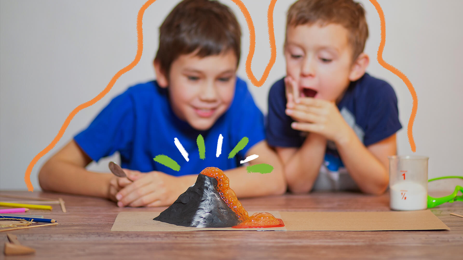 Na foto, dois meninos olham para um vulcão caseiro, que derruba lava na cor laranja. Os meninos têm pele clara e usam camisetas azuis.