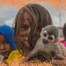 Três crianças indígenas posam para foto, uma delas segura um macaquinho