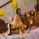 Uma menina de costas e camiseta branca reza diante de um altar montado em casa com a imagem de Nossa Senhora