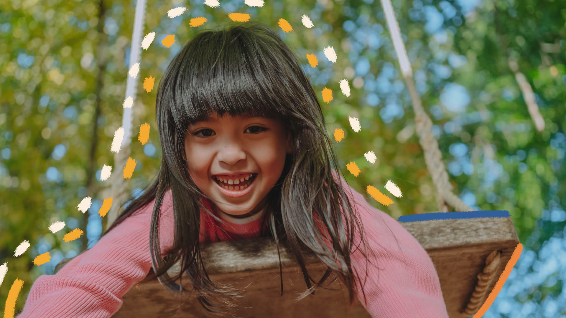 Na foto, uma menina de pele clara e cabelos escuros sorri enquanto brinca em um balanço.