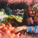 Na foto, mãe e filho selecionam tomates em uma feira livre. Ambos têm pele clara e sorriem enquanto escolhem. A imagem possui uma intervenção de moldura na cor rosa.