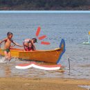 Quatro crianças brincam em dia de sol à beira do Velho Chico, há dois barcos - um amarelo e um azul - e um coco verde na areia