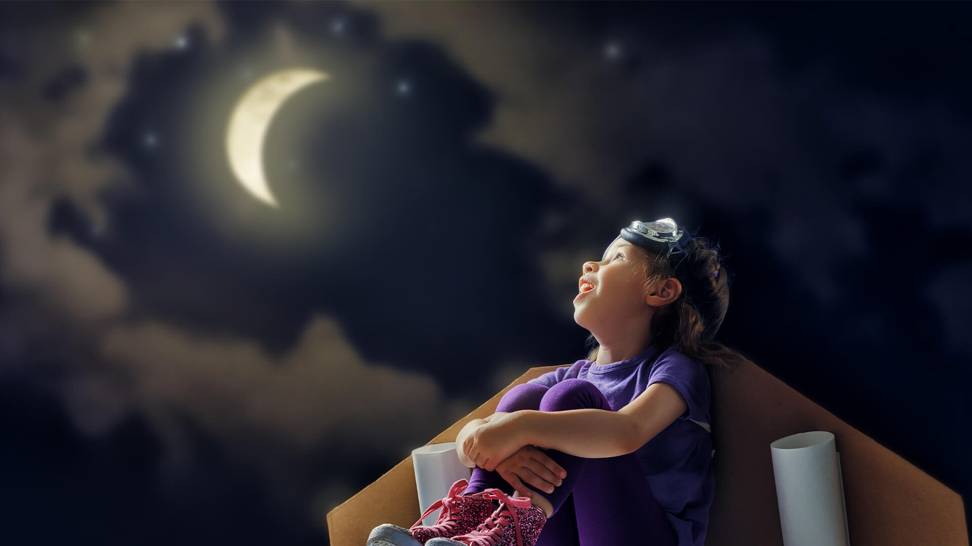Uma criança sentada no chão segurando os joelhos olha para a lua