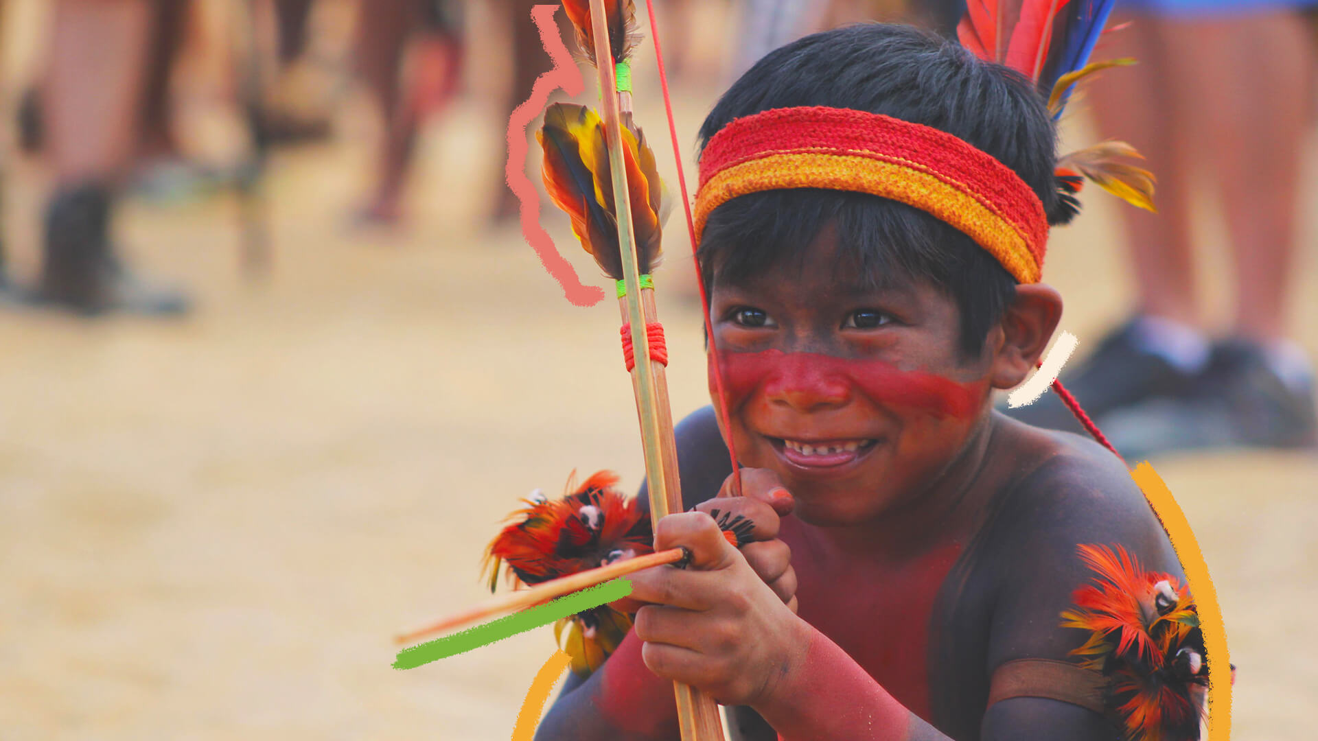 Na foto, um menino indígena sorri enquanto segura um arco e flecha. A imagem possui intervenções coloridas.