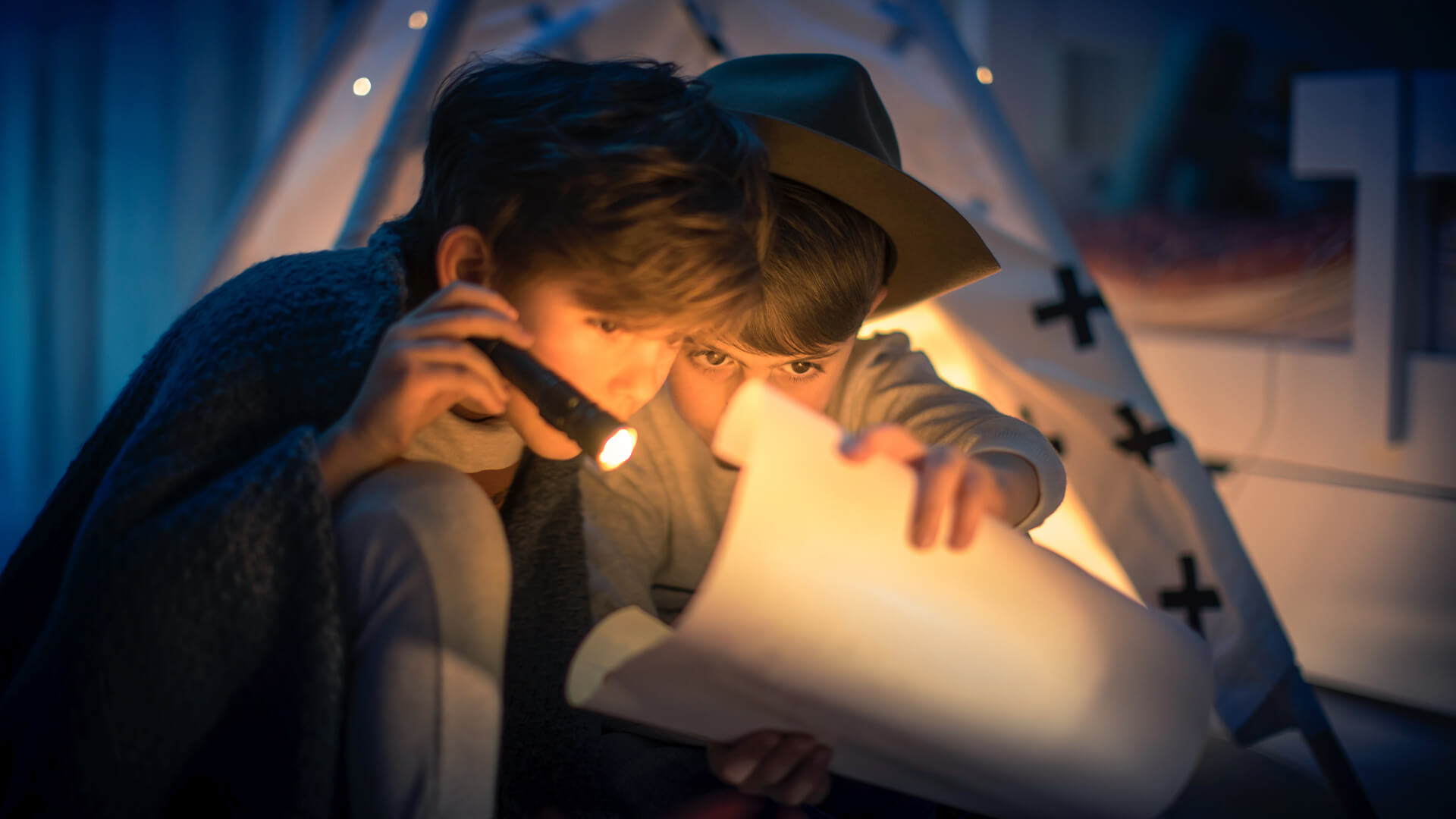 Duas crianças olham um mapa no escuro com a ajuda de uma lanterna