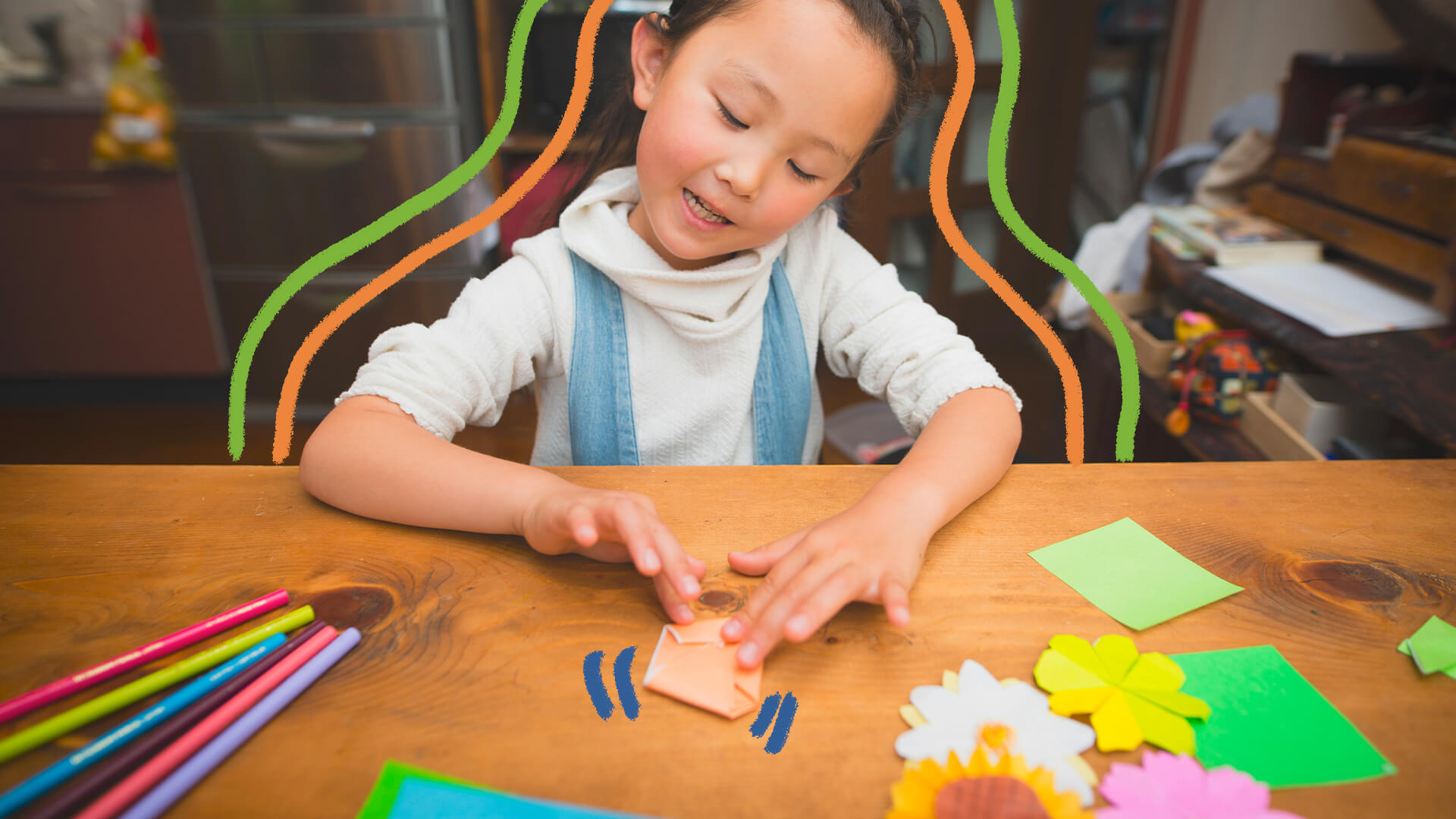 Na foto, uma criança de descendência asiática dobra um origami em uma mesa de madeira.