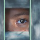 No centro da foto, por entre as grades de uma janela, há um olho de criança. A matéria é sobre o aumento de números de casamento infantil na pandemia.