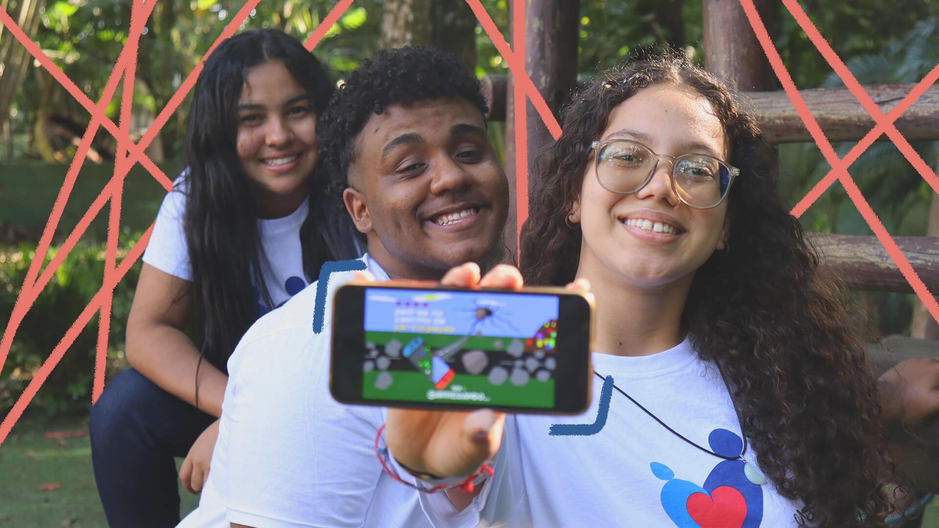 Na foto, três adolescentes sorriem enquanto mostram a tela de um celular, que mostra um jogo.