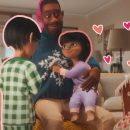 Na foto, cena da animação "Pai de coração". Mike abraça sua enteada enquanto sua companheira sorri. A imagem possui intervenções de corações desenhados.
