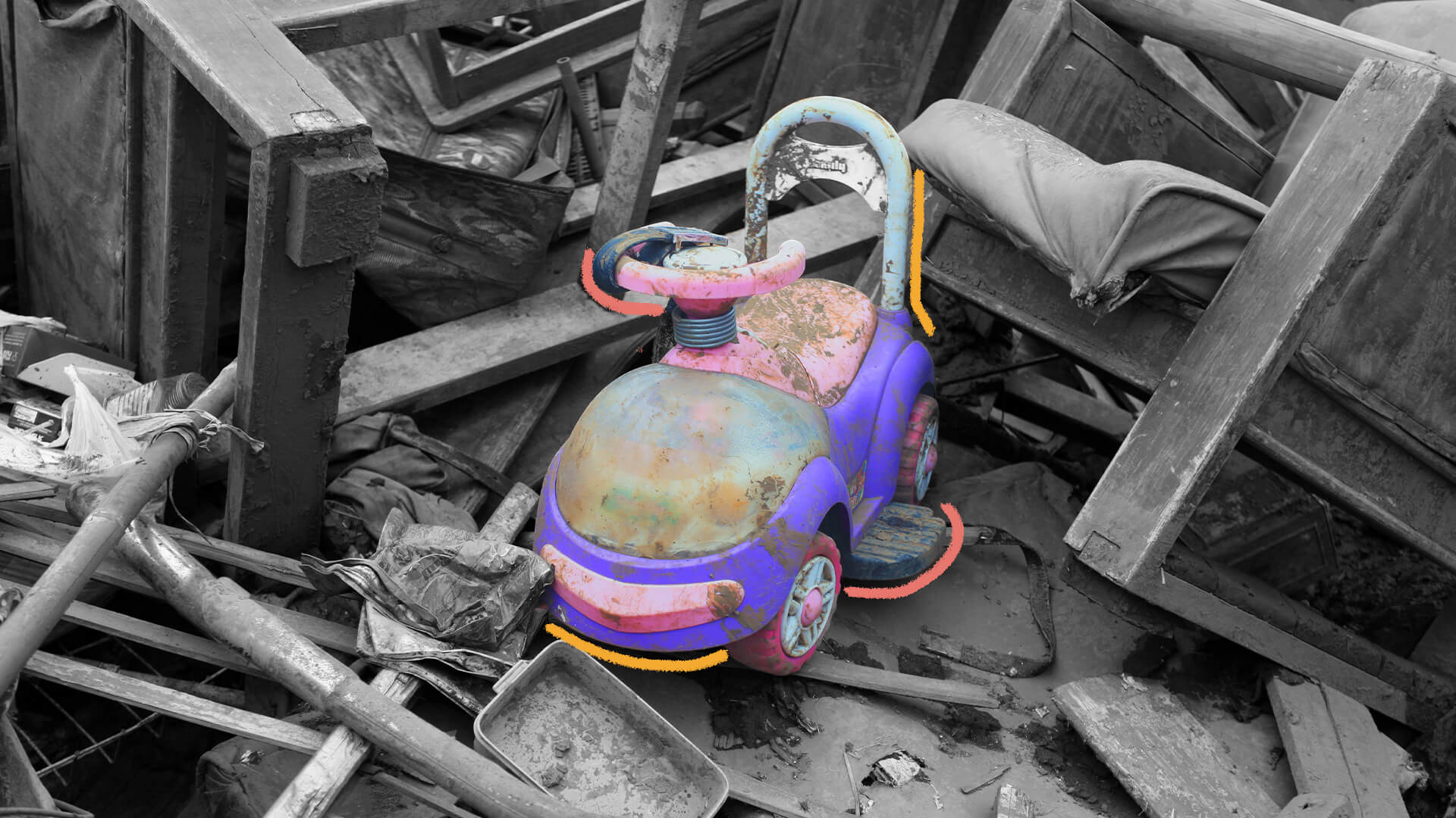 Um carrinho de brinquedo está em destaque, em cores, em meio a casas destruídas, em preto e branco