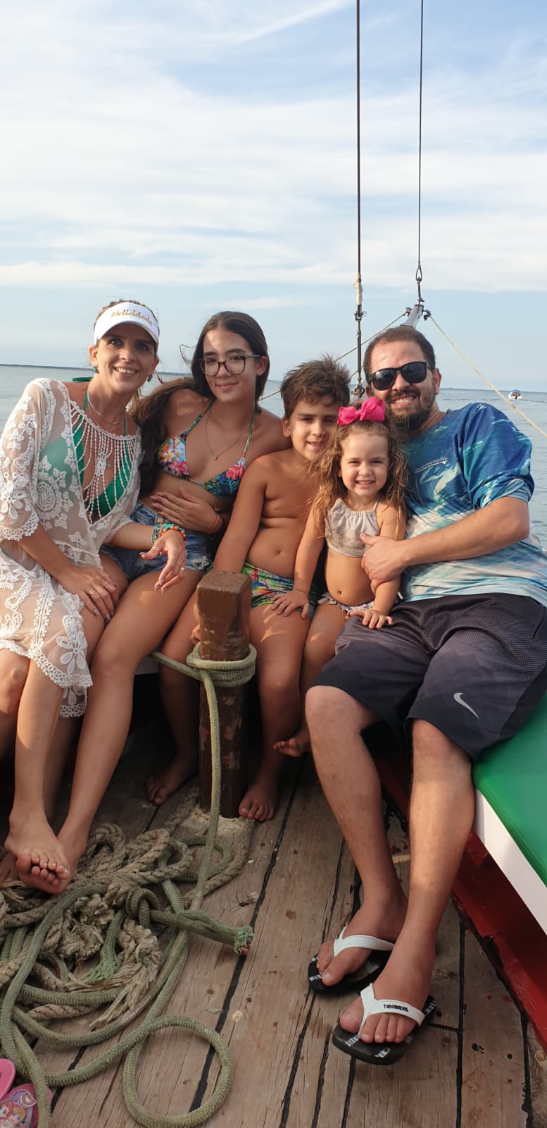 Uma família (um casal e três filhos) posa para a foto em um barco, em trajes de banho