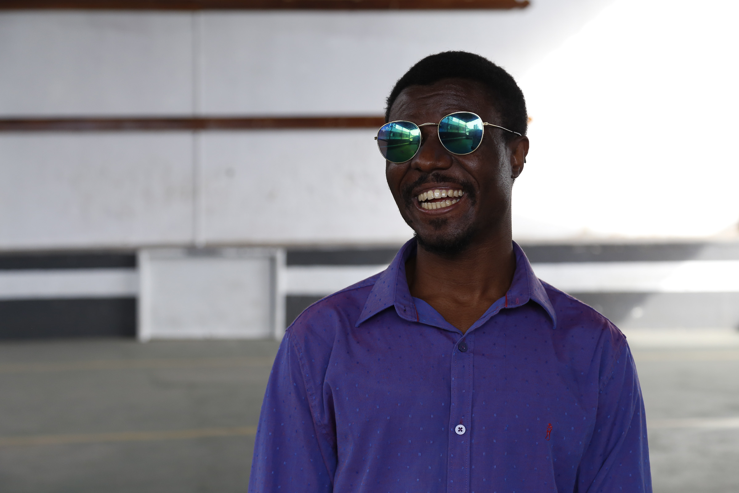 Foto de um homem negro usando óculos de lentes espelhadas e camisa azul. Ele está numa quadra esportiva.