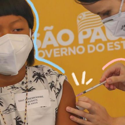 Foto com funda amarelo mostra menino indígena de máscara, em primeiro plano, recebe vacina aplicada no braço por profissional de saúde.