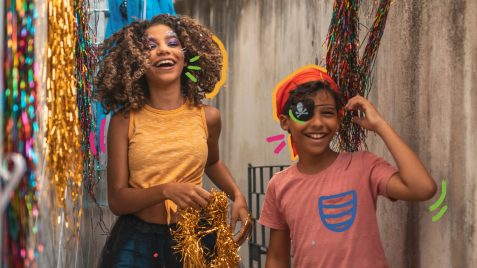 5 passos para fazer um carnaval em casa com as crianças: na imagem, duas crianças seguram confetes e adornos para fantasias de carnaval.