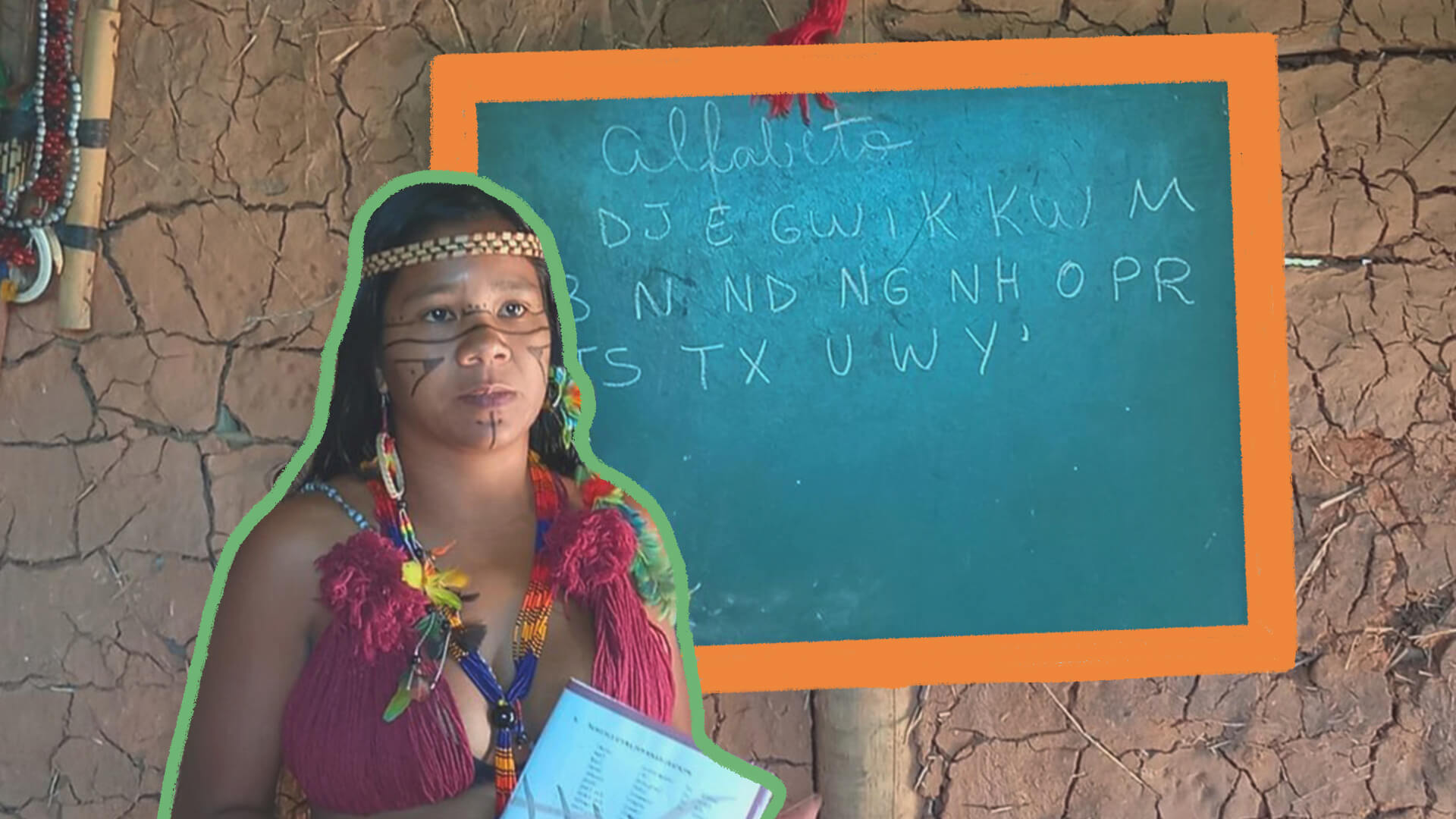 Na foto, a educadora indígena Guaciane está na frente de uma lousa. Ela tem pele escura e seu rosto possui grafismos indígenas. A lousa mostra letras do alfabeto tupi-guarani.