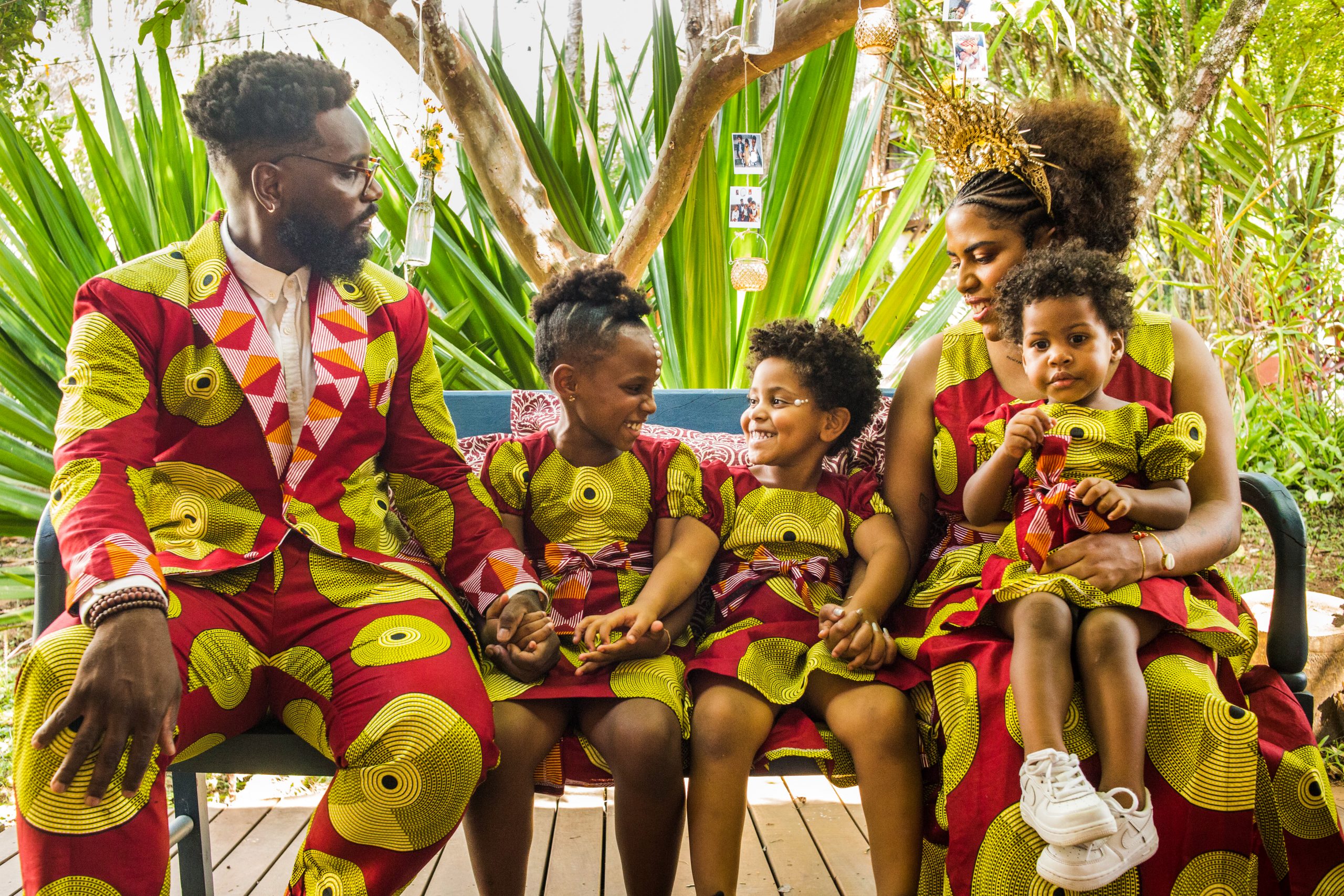 Uma família com três filhas. Os adultos e as crianças vestem a mesma estampa em vermelho e amarelo. Todos são negros