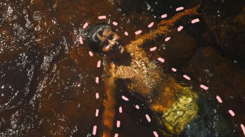 Na foto, uma criança de pele escura aparece sorrindo enquanto brinca mergulhada em um rio. a imagem possui intervenções de rabiscos coloridos na cor rosa.