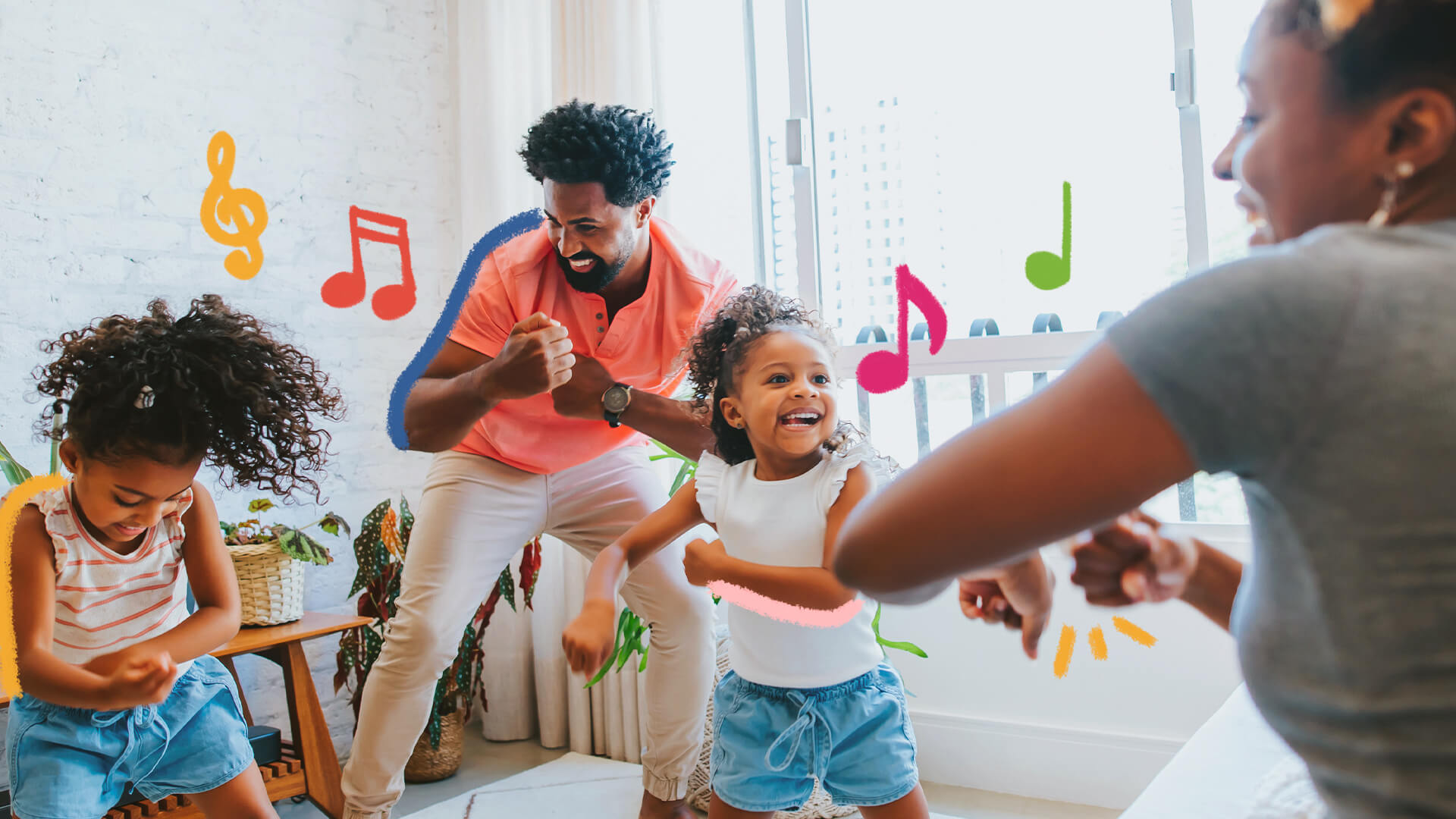 Uma família de pessoas negras (dois adultos e duas meninas) dançam na sala de casa