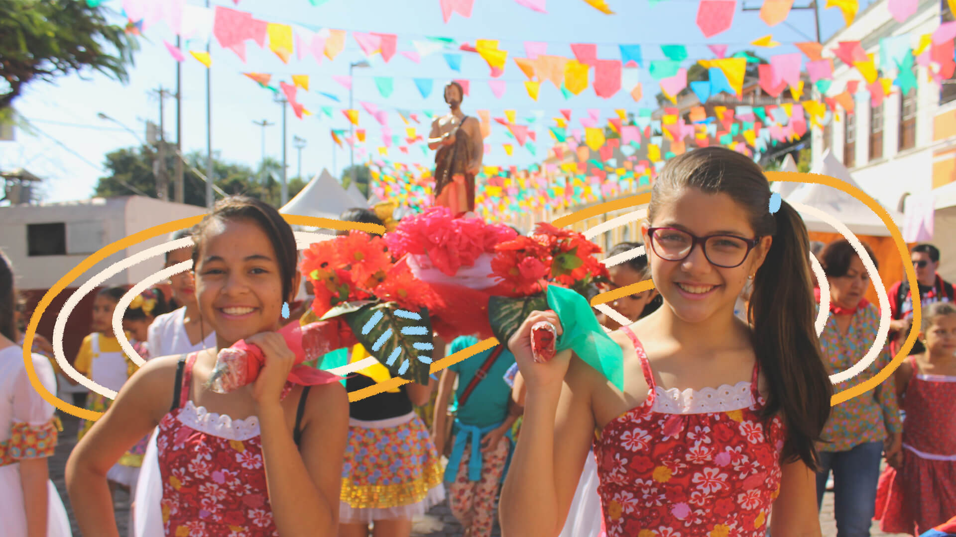 Duas meninas de vestidos floridos em vermelho iguais seguram o andor de São João ornamentado com flores vermelhas