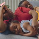 Na imagem, uma mãe está deitada no sofá com a filha e o filho. Todos são negros e mantêm semblantes cansados. A imagem possui intervenções de rabiscos coloridos.