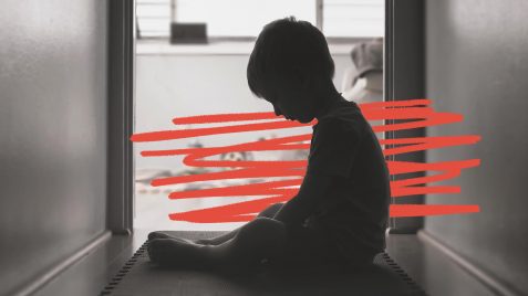 Imagem em preto e branco de um menino sentado no chão, olhando para baixo. A foto mostra sua silhueta contra a luz. A imagem possui intervenções de rabiscos vermelhos.