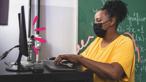 Na imagem, uma professora negra utiliza um computador em uma sala de aula. Atrás dela há uma lousa. A imagem possui intevenções de rabiscos coloridos.