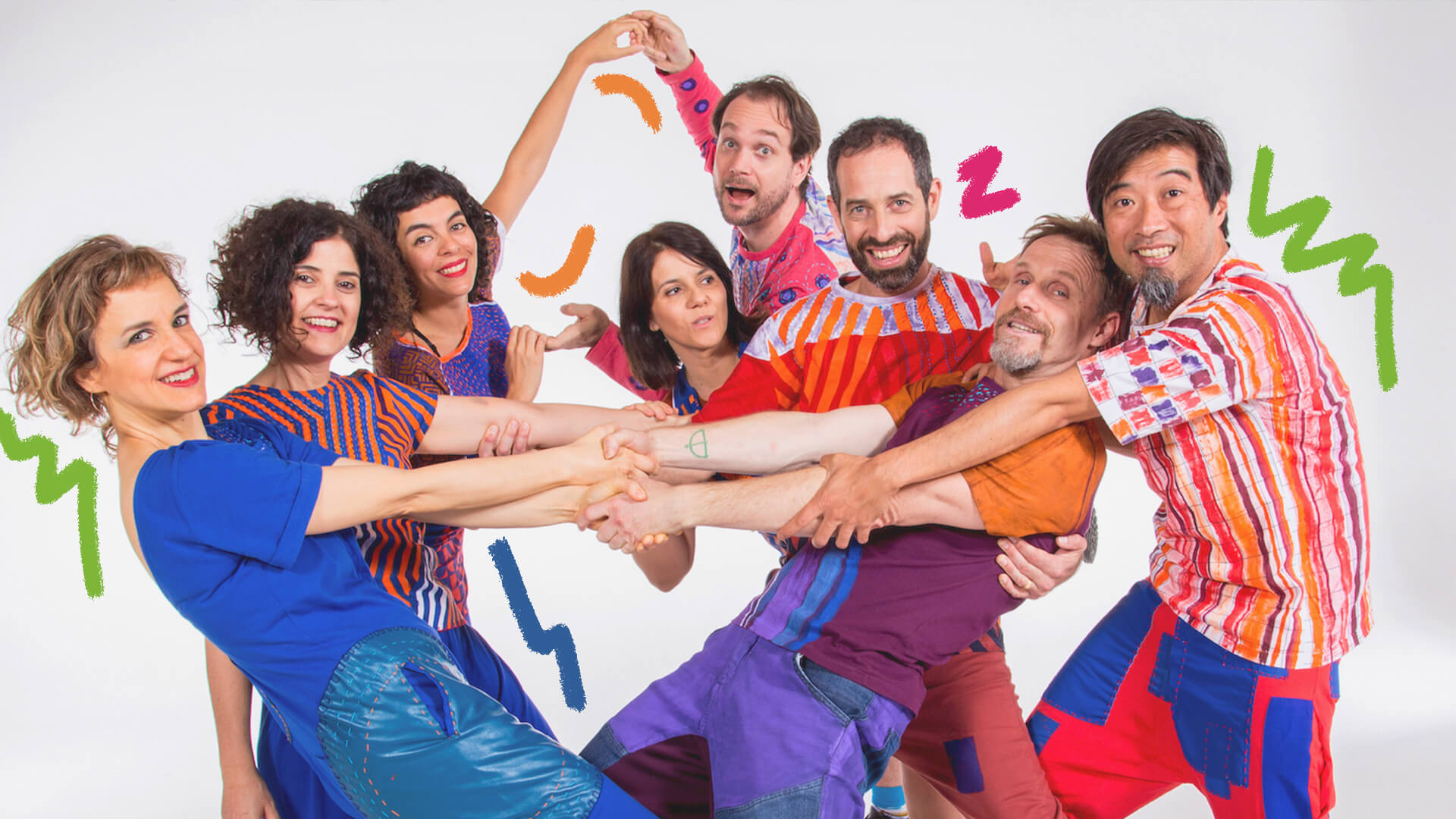 Foto do grupo Barbatuques: homens e mulheres vestem roupas coloridas, alguns se dão as mãos e posam com movimentos de corpo diferentes