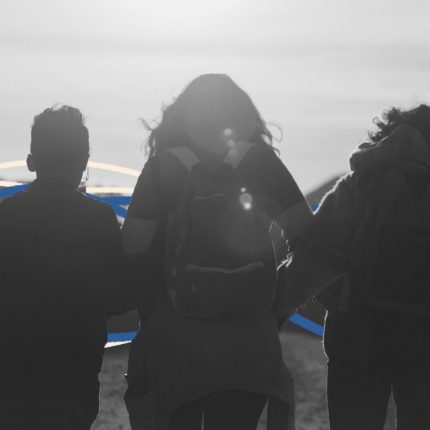 Imagem de costas de uma mulher caminhando por uma estrada de mãos dadas com duas crianças
