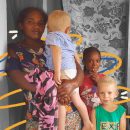 Foto de uma família quilombola: a mãe e a filha mais velha são negras e os dois meninos são negros albinos. Eles vestem roupas coloridas e o fundo da foto está em preto e branco