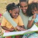 Duas meninas negras leem um livro com uma mulher negra. A imagem possui rabiscos coloridos e ilustra uma matéria sobre autoras negras para conhecer no Dia Internacional da Mulher Negra Latino-americana e Caribenha.